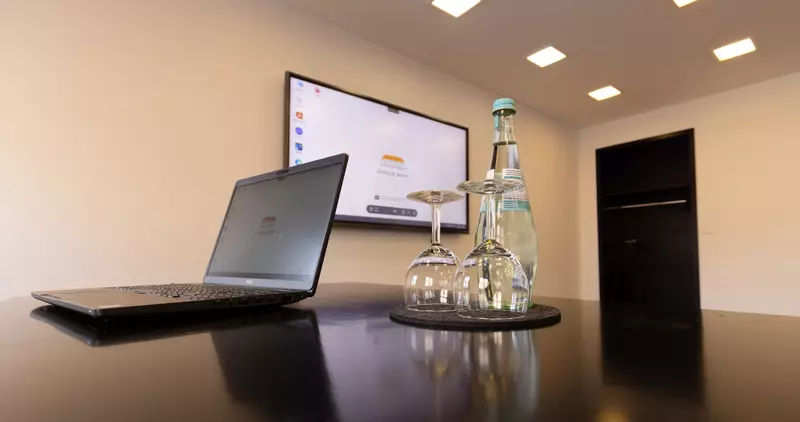 Martini-Raum mit TFT-Bildschirm, Laptop, Gläsern und Wasserflasche am Tisch